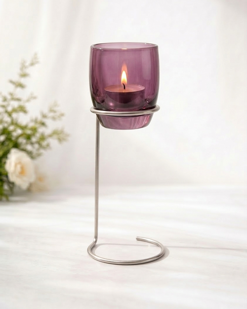 Purple candle holder with a lit candle on a white surface, with a blurred background
